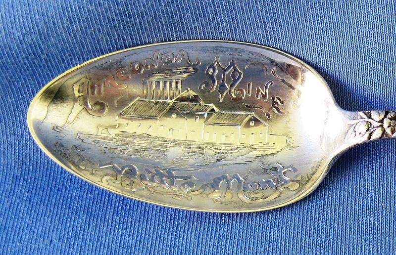 Souvenir Mining Spoon Anaconda  Mine Closeup.JPG - SOUVENIR MINING SPOON ANACONDA MINE - Sterling silver spoon embossed with a detailed picture of the Anaconda Mine Butte Montana; with floral design on handle, 5 3/4 in long, marked on back Sterling with a mfg. hallmark  (The Anaconda Copper Mine was the largest copper-producing mine in the world from 1892 through 1903.  Located in Butte, Montana it transformed this small and poor town into one of the most prosperous cities in the country, often called the Richest Hill on Earth.  This small silver mine was bought in 1881 by Marcus Daly from Michael Hickey. Hickey was a prospector and Union Civil War veteran, and named his claim the Anaconda Mine after reading Horace Greeley's Civil War account of how Ulysses S. Grant's forces had surrounded Robert E. Lee's forces "like an anaconda". Daly then developed the Anaconda Mine in partnership with George Hearst, father of William Randolph Hearst, and James Ben Ali Haggin and Lloyd Tevis of San Francisco.  Huge deposits of another mineral, copper, were soon discovered.  Daly quietly bought up neighboring mines forming a mining company and would eventually own all the mines on Butte Hill. He then built a smelter at Anaconda which he connected to Butte by a railway. From this beginning grew the Anaconda Copper Mining Company, a global mining enterprise featuring the Anaconda and other Butte mines, a smelter at Anaconda, Montana, processing plants in Great Falls, Montana, the American Brass Company, and many other properties, mostly in the United States and Chile. The Anaconda Copper Mining Company was acquired by ARCO in 1977.  The Anaconda mine itself was closed in 1947 after producing 94,900 tons of copper. Its location has been consumed by the Berkeley Pit, a vast open-pit mine.  In 1977, Anaconda was sold to the Atlantic Richfield Company (ARCO) for $700 million.  By 1983 the Berkeley Pit was completely idle and ARCO suspended all operations in Butte.)